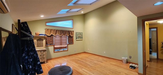 interior space with recessed lighting, an AC wall unit, wood finished floors, vaulted ceiling with skylight, and baseboards