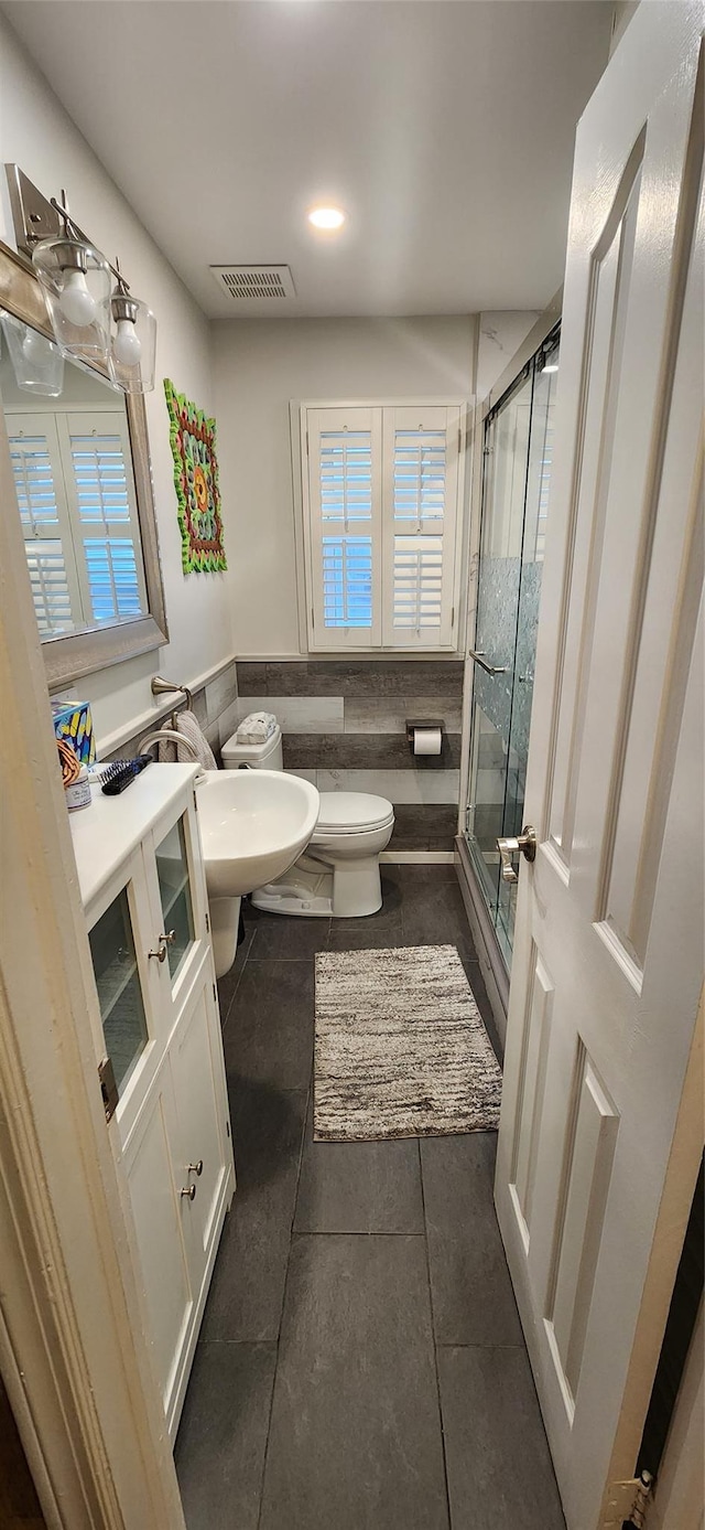 bathroom featuring tile walls, visible vents, toilet, a stall shower, and wainscoting