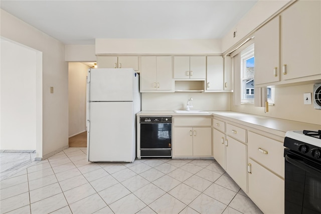 kitchen featuring black dishwasher, light countertops, cream cabinets, freestanding refrigerator, and a sink