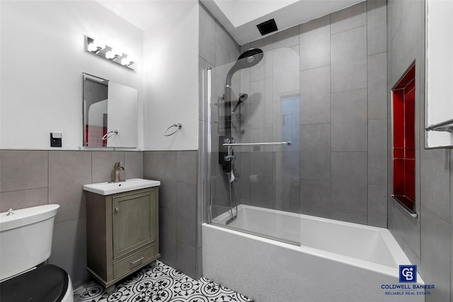 bathroom featuring tile patterned flooring, toilet, vanity, tile walls, and  shower combination