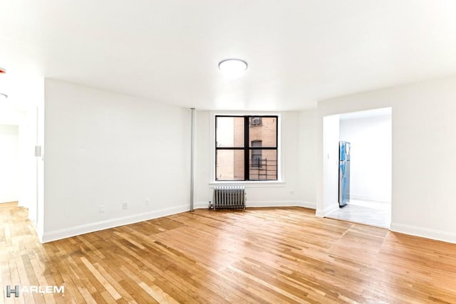 spare room featuring radiator, baseboards, and light wood finished floors