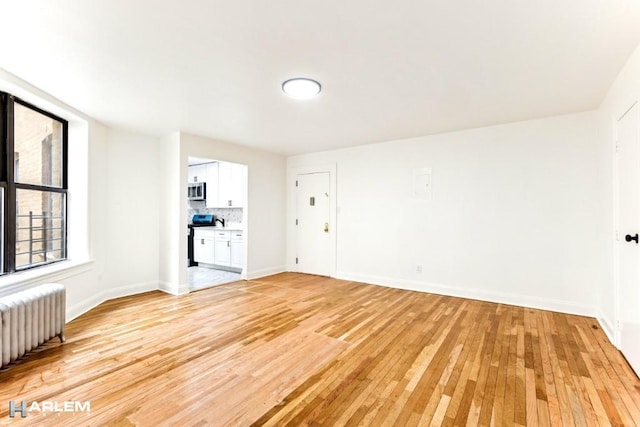 empty room with baseboards, light wood-style floors, and radiator