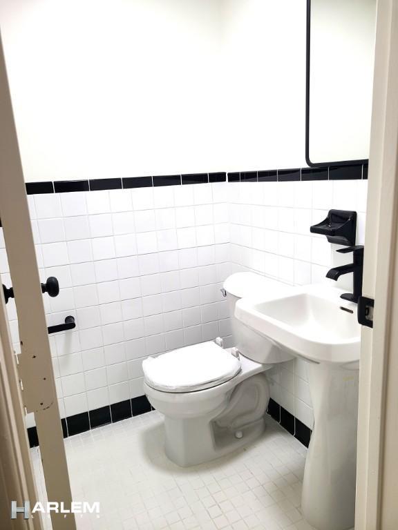 bathroom featuring tile patterned flooring, toilet, and tile walls