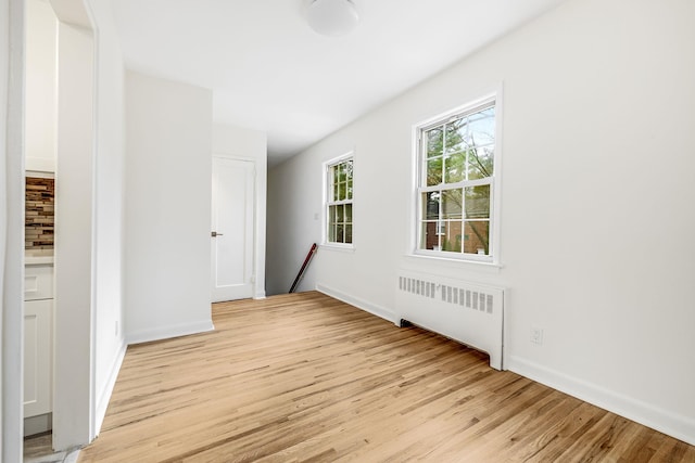 unfurnished room with baseboards, light wood-style flooring, and radiator heating unit