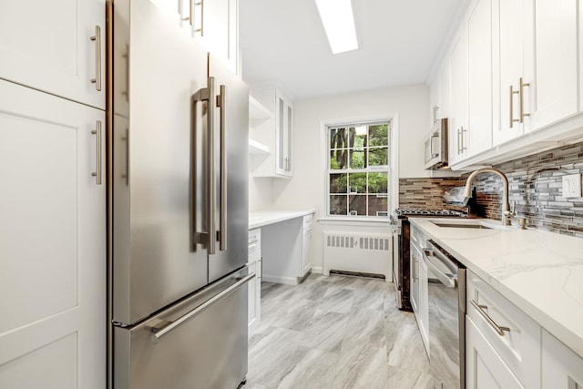 kitchen featuring radiator, a sink, white cabinets, appliances with stainless steel finishes, and backsplash