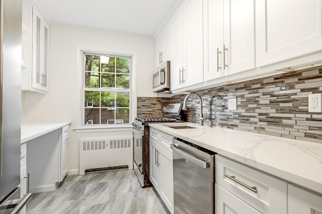 kitchen with backsplash, appliances with stainless steel finishes, white cabinets, and radiator heating unit