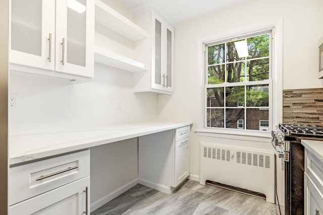 kitchen with light stone counters, white cabinetry, radiator, glass insert cabinets, and stainless steel range with gas stovetop