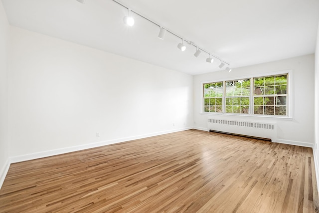 empty room featuring light wood finished floors, radiator heating unit, and baseboards