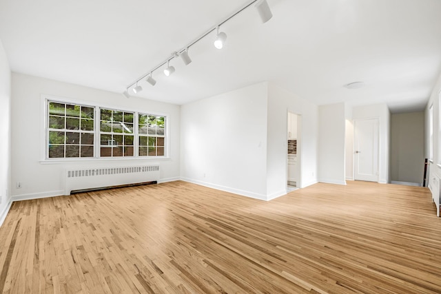 empty room featuring light wood-style floors, baseboards, and radiator