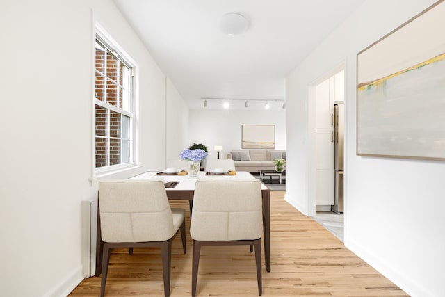 dining area featuring rail lighting, light wood-style floors, and baseboards