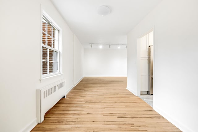 hallway with light wood-style flooring, rail lighting, radiator heating unit, and baseboards