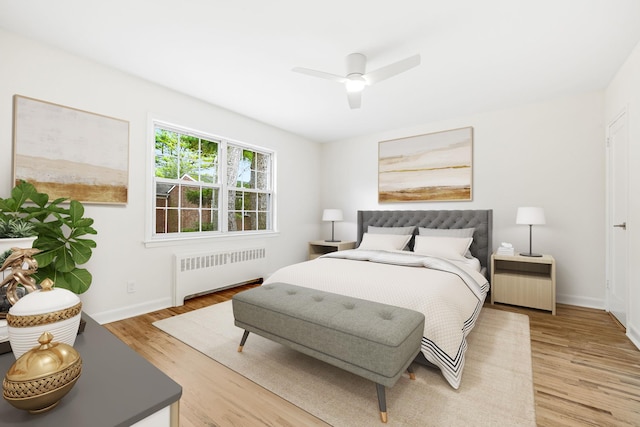 bedroom featuring light wood-style flooring, radiator heating unit, a ceiling fan, and baseboards