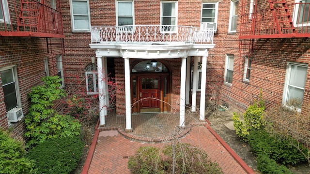 property entrance with cooling unit, brick siding, and a balcony