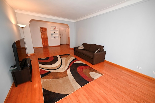 living area featuring arched walkways, crown molding, baseboards, and wood finished floors