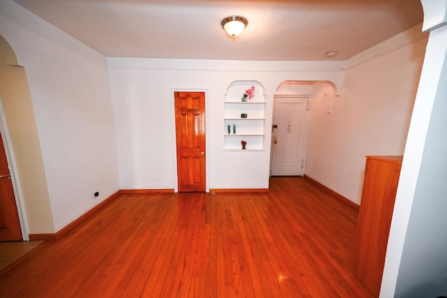 spare room featuring built in features, arched walkways, baseboards, and wood finished floors