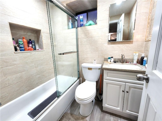 full bathroom with toilet, shower / bath combination with glass door, wood finished floors, vanity, and tile walls
