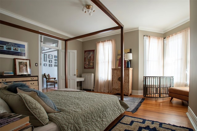 bedroom with ornamental molding, radiator heating unit, wood finished floors, and baseboards
