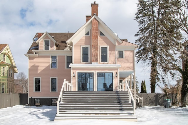 snow covered back of property featuring stairway, fence, and a chimney