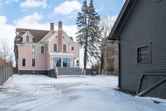 snow covered property with fence, stairway, and a chimney