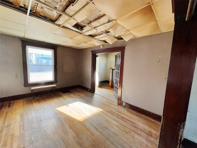 spare room featuring wood-type flooring, a drop ceiling, and baseboards