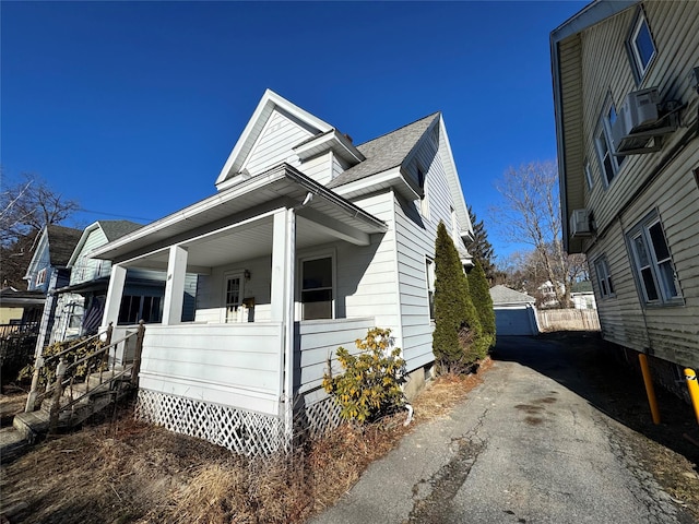 view of property exterior featuring covered porch, a shingled roof, and an outdoor structure