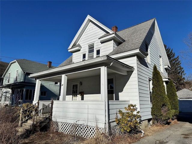 bungalow-style house with covered porch, a shingled roof, and a chimney