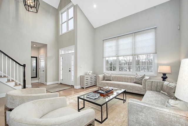 living area featuring a notable chandelier, a towering ceiling, baseboards, stairs, and light wood finished floors