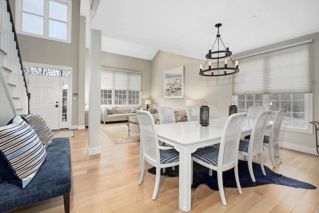 dining space featuring lofted ceiling, a notable chandelier, baseboards, light wood-style floors, and stairway