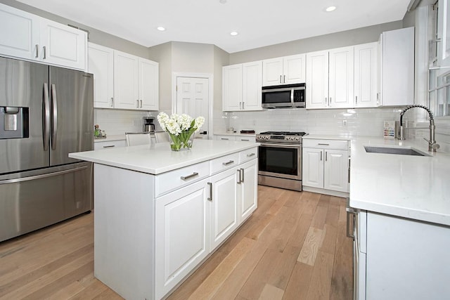 kitchen featuring light wood finished floors, a center island, stainless steel appliances, white cabinetry, and a sink