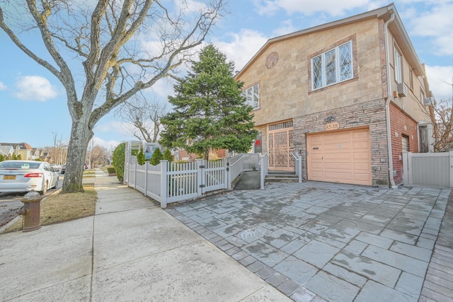 view of front facade with an attached garage, a gate, fence, stone siding, and driveway