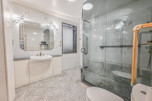 bathroom featuring a stall shower, vanity, toilet, and tile walls