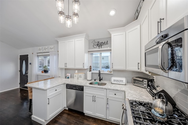 kitchen with appliances with stainless steel finishes, white cabinets, a sink, and a peninsula