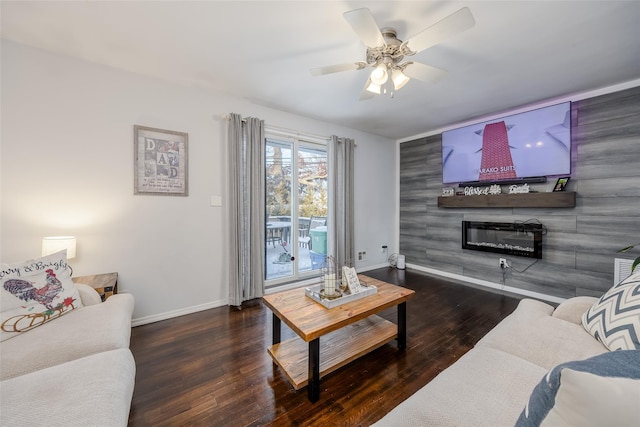 living area featuring a glass covered fireplace, ceiling fan, baseboards, and wood finished floors