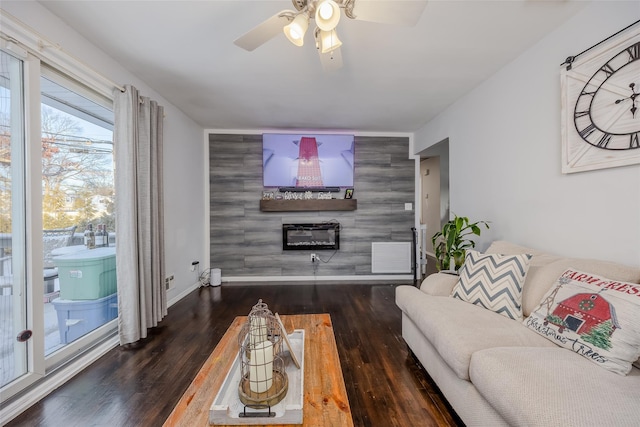 living room featuring an accent wall, a glass covered fireplace, wood finished floors, and baseboards