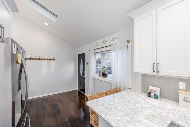 kitchen with light countertops, backsplash, lofted ceiling with skylight, freestanding refrigerator, and white cabinets