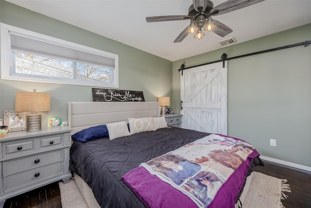 bedroom with ceiling fan, a barn door, visible vents, baseboards, and dark wood finished floors