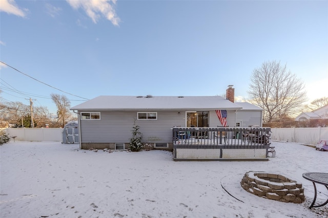 snow covered house with a storage unit, a fenced backyard, a fire pit, and a wooden deck