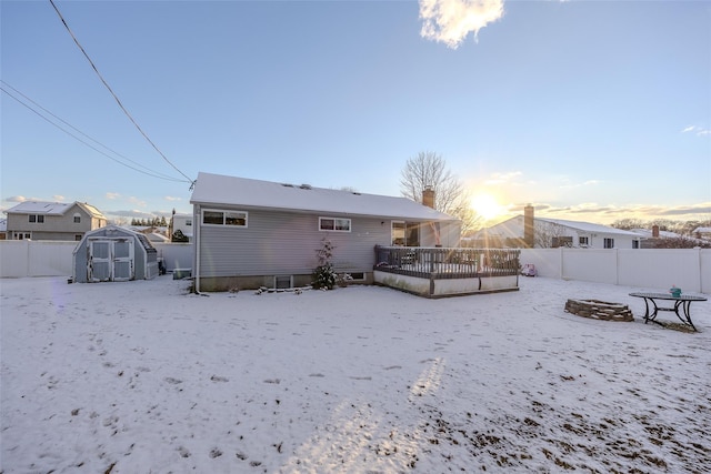 snow covered house featuring a fenced backyard, an outdoor structure, a chimney, and a storage shed