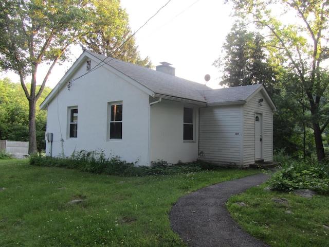 view of side of home featuring stucco siding, a shingled roof, a chimney, and a yard