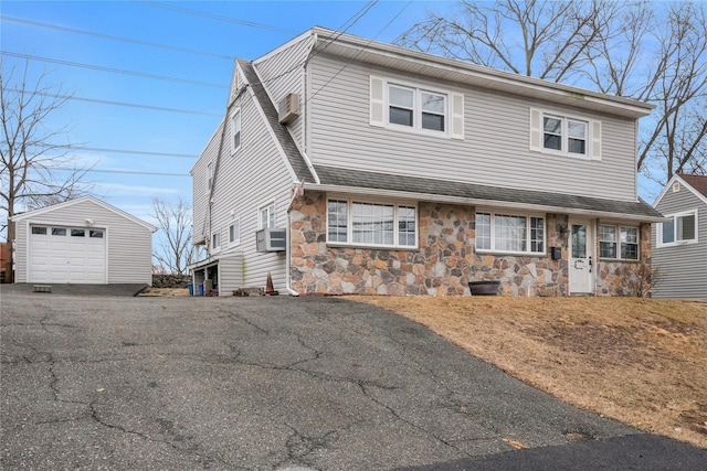 view of front of house with an outbuilding, aphalt driveway, stone siding, a detached garage, and a shingled roof