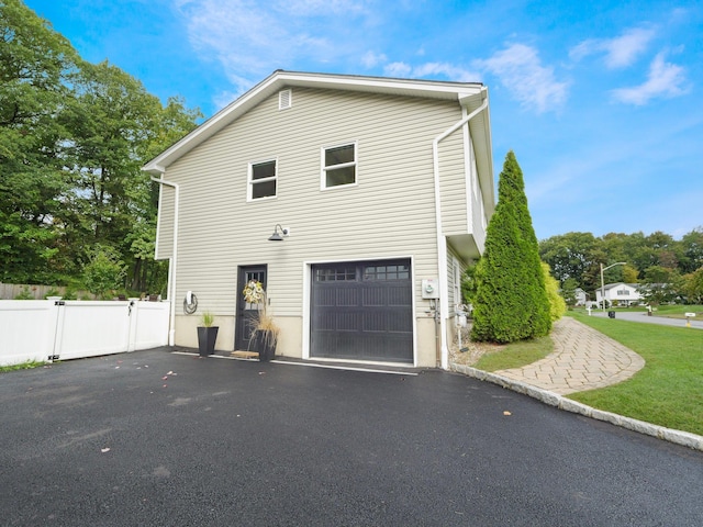 view of side of property featuring driveway, an attached garage, and fence