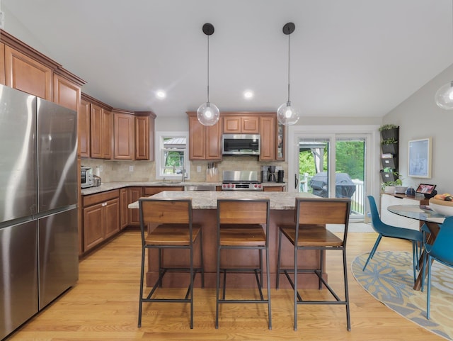 kitchen featuring a sink, appliances with stainless steel finishes, light wood-type flooring, decorative backsplash, and light stone countertops