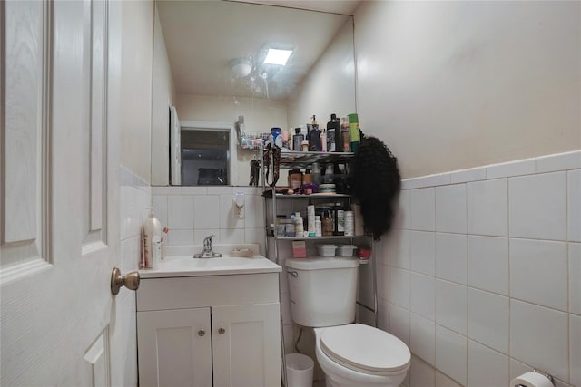 half bathroom featuring vanity, toilet, and tile walls