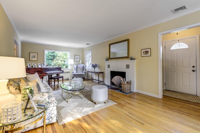 living room with visible vents, a brick fireplace, wood finished floors, and ornamental molding