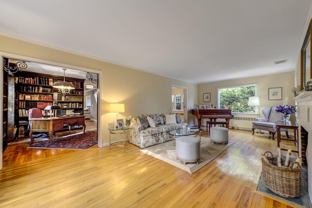 living room with visible vents, a notable chandelier, hardwood / wood-style floors, radiator heating unit, and crown molding