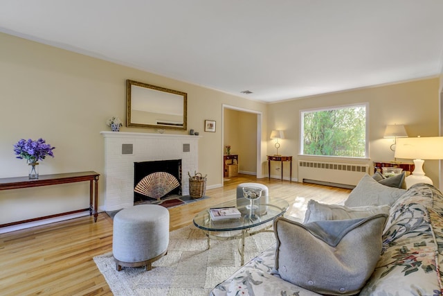 living area featuring a brick fireplace, radiator, and wood finished floors