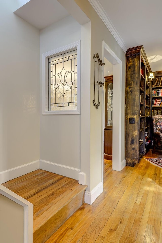 hallway featuring light wood finished floors, crown molding, and baseboards