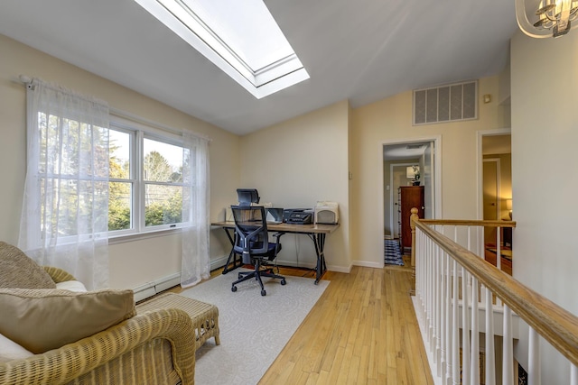 home office featuring light wood finished floors, visible vents, baseboards, vaulted ceiling with skylight, and a baseboard radiator