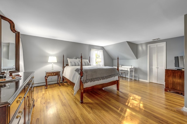 bedroom with visible vents, light wood finished floors, a baseboard radiator, lofted ceiling, and a baseboard heating unit