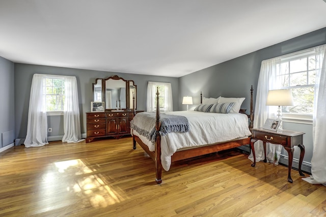 bedroom with light wood-type flooring, baseboards, baseboard heating, and a baseboard heating unit